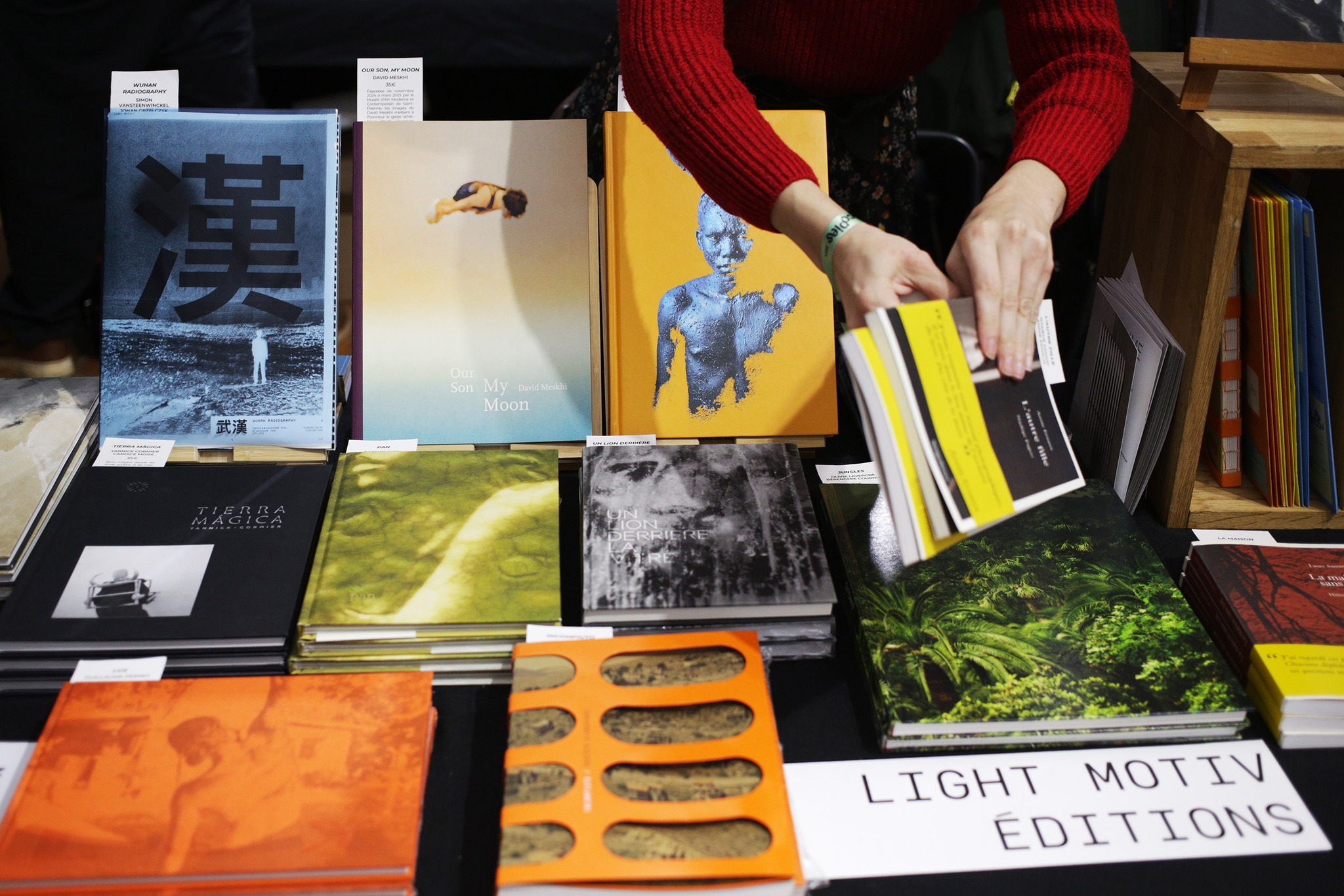 Une personne récupère deux livres dans ses mains, juste au-dessus d'une table recouverte des ouvrages photographiques des Editions Light Motiv lors du salon Polycopies à Paris en novembre 2024.